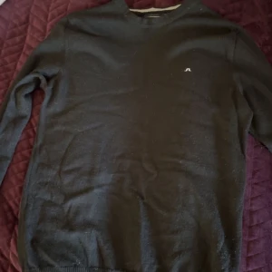 Svart stickad tröja från J.Lindeberg - Svart stickad tröja från J.Lindeberg i storlek M. Klassisk rund hals och diskret logga på bröstet. Mjuk och skön känsla, perfekt för kyliga dagar. Passar dig som gillar stilrena och enkla plagg med snygg passform.