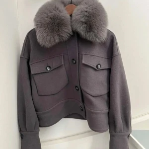 Meotine jacka - Snygg grå overshirt med oversized passform och stora fickor framtill. Jackan har en maffig, fluffig pälskrage som ger en lyxig vibe. Stängs med knappar och har långa ärmar med breda muddar. Perfekt för dig som vill sticka ut i höst och vinter.