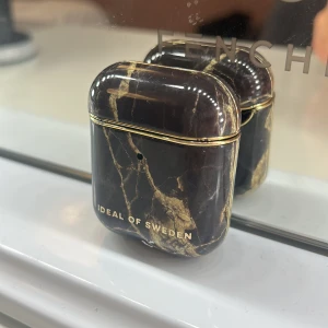 Svart marmormönstrat AirPods-fodral - Snyggt AirPods-fodral från iDeal of Sweden i svart med marmormönster och guldiga detaljer. Fodralet har en lyxig vibe med sitt blanka yttre och stilrena design. Perfekt accessoar för dig som vill ha något unikt och trendigt till dina hörlurar.