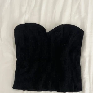Svart ribbad stickad tubtopp - Säljer en svart ribbad stickad tubtopp med hjärtformad överkant. Toppen är croppad och sitter tight, perfekt att styla med höga jeans eller kjol. Enkel men ändå snygg detalj till din outfit.