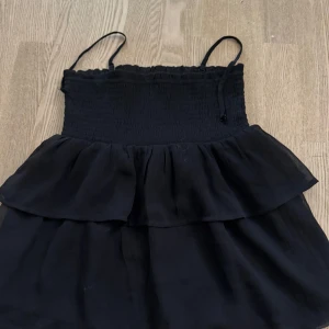 Svart volangtopp Gina Tricot - Supersöt svart volang topp från Gina Tricot med smockad överdel och tunna axelband. Går att matcha lätt!