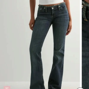 Bootcut jeans i mörkblå denim - Snygga bootcut jeans i mörkblå tvätt med klassisk femficksdesign och låg midja. Jeansen har raka ben som blir vidare nedtill och detaljer som knappar och dragkedja framtill. Perfekta för dig som gillar en retro vibe och vill ha ett par jeans med cool passform.