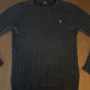 Mörkblå kabelstickad, Gant - Kabelstickad mörkblå tröja från Gant med rund hals och diskret logga på bröstet. Använd ett par gånger bara då den inte kommit till användning. Ljuset på bilden är lite dålig och kan upplevas att tröjan har ljusare områden på några ställen av tröjan, bara att be om fler bilder isåfall! Pris går alltid att diskutera, bara att höra av dig.