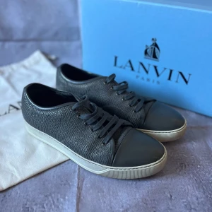 Lanvin Paris Cap-Toe Sneakers – Strl UK 8 / EU 42 – Svart läder med lacktå – Med låda & dustbag - Säljer ett par exklusiva Lanvin Paris Cap-Toe Sneakers i svart präglat läder med lackad tå.  🎨 Färg: Svart med svart lacktå och vit yttersula 📏 Storlek: UK 8 / EU 42 📐 Mått: Innermått ca 27 cm (normal passform för EU 42) ♻️ Skick: 9/10 🧵 Material: Präglat läder med lacktå i skinn, gummisula, textilfoder och snören