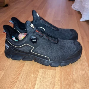 Svarta sneakers från Helly Hansen - Svarta sneakers från Helly Hansen/JOBB SKOR med BOA-snörningssystem och grov platt sula. Ovandelen är i slitstark syntet med diskreta vita detaljer och röd söm. Skorna har rund tå och reflekterande dragflik bak. Perfekta för dig som gillar sportig och clean stil till jobbet:) Nästan helt nya använda Max 3 gånger 
