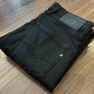 Svarta Replay Anbass jeans - Säljer ett par svarta Replay Anbass jeans med klassisk femficksdesign och svarta sömmar. Byxorna är i extremt fint skick utan skador✅. Perfekta för dig som gillar stilrena svarta jeans. Storlek W32 L34.