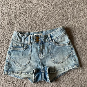 Ljusblå jeansshorts från Lindex - Säljer ett par ljusblå jeansshorts från Lindex med dubbla knappar och broderade detaljer på fickorna.  Shortsen är låg midjade och perfekta för varma dagar! Säljer dem då dem är försmå för mig ❤️