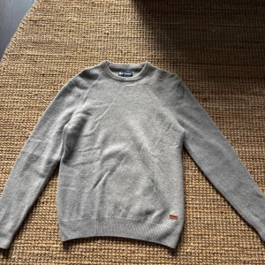 Grå/beige ulltröja från Barbour med mockadetaljer - Säljer en stilren grå ulltröja från Barbour i storlek M med mocka detaljer på armbågarna. 