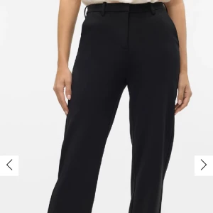 Svarta kostymbyxor med normal passform - Säljer ett par klassiska svarta kostymbyxor med raka ben och hällor för bälte. Byxorna har diskreta fickor i sidorna och stängs med dragkedja och knapp. Perfekta för en stilren look.