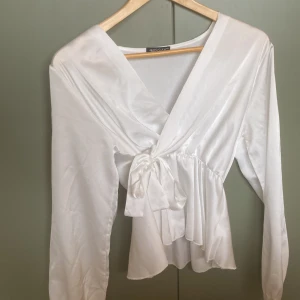 Vit omlottblus med knyt från Missay - Säljer en elegant vit omlottblus från Missay med lång ärm och knyt i midjan. Blusen har v-ringning och ett fint fall i tyget, perfekt för en stilren look. Justerbar i midjan.❤️