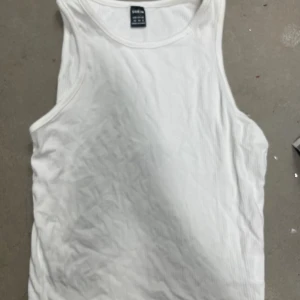 Vit ribbad linnetopp från SHEIN - Säljer en klassisk vit ribbad linnetopp från SHEIN i storlek XS. Perfekt att styla till jeans eller shorts. Enkel och tidlös design med rund halsringning och ärmlös modell.
