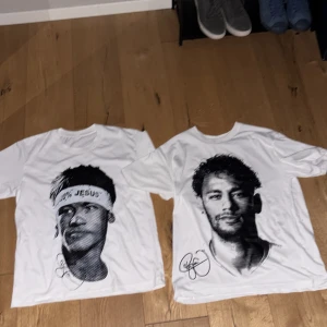 Vita t-shirts med porträtttryck - Två vita t-shirts med stora svartvita porträtttryck framtill. Den ena har ett porträtt av en person med pannband där det står '100% JESUS', den andra har ett porträtt av en man med skägg. Båda har rund hals och korta ärmar.