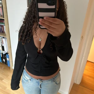 Svart croppad topp festtopp med v-ringning  - Svart croppad topp med djup v-ringning och långa ärmar. Toppen har öppning framtill och en figurnära passform. Perfekt att styla med jeans eller kjol.