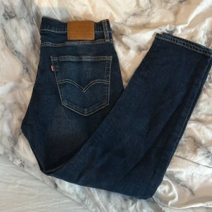 Mörkblå Levis jeans - Säljer ett par klassiska mörkblå Levis jeans med raka ben och snygga kontrastsömmar. Byxorna har en bakficka med Levis-logga och läderpatch i midjan. Perfekta för alla stilar.
