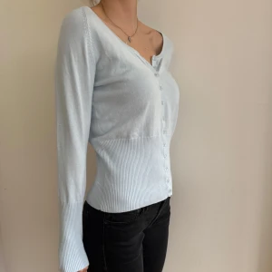 Ljusblå kofta  - Säljer en ljusblå kofta från Tippy och knappar framtill. Koftan har lång ärm och ribbade partier vid ärmslut och midja för en snygg passform. 