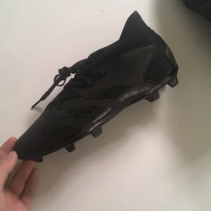 Svarta adidas predators  - Säljer ett par helsvarta adidas predators med snörning och mönstrad sula för extra grepp. Skorna har en låg profil och är tillverkade i syntetmaterial. Perfekta för dig som vill ha en stilren look på planen.