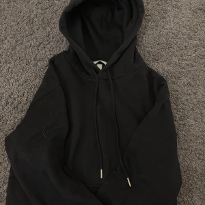 Svart hoodie i storlek XS - En klassisk svart hoodie med huva och dragsko. Perfekt för en avslappnad stil och enkel att matcha med det mesta. Hoodien har en känguruficka framtill och långa ärmar.💞