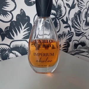 Fabio Verso Imperium Absolue Eau de Parfum - En elegant parfymflaska med svart lock och genomskinligt glas som visar den bärnstensfärgade vätskan. Doften heter Imperium Absolue och är en Eau de Parfum. Flaskan har en modern, droppformad design och passar perfekt på parfymhyllan. Jag fick den av min bror men jag har inte använt det så mycket 😁
