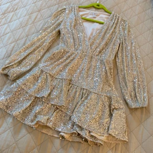Glittrig silverklänning med volang och v-ringning - Säljer en superfin glittrig silverklänning med v-ringning och långa ärmar. Klänningen har volangdetaljer och är täckt av paljetter som ger en riktigt festlig look. Perfekt för dig som vill sticka ut på festen🥂🩷