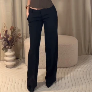 Svarta kostymbyxor med normal passform - Snygga svarta kostymbyxor med raka, vida ben och klassisk design. Byxorna har fickor i sidorna och stängs med dragkedja och knapp framtill. Perfekta för en stilren och trendig look.