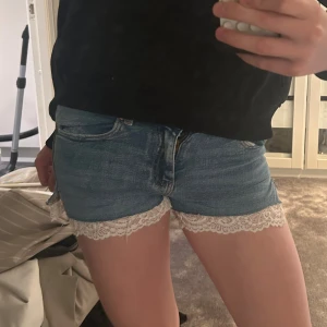Blå jeansshorts med spetskant - Snygga blå jeansshorts med vit spetskant längst ner. Klassisk femficksmodell med normal passform och låg midja. Perfekta för sommaren och ger en söt touch med spetsdetaljen. Storlek 146 men passar xs, jag har gjort de själva med ett par avklippta beans från Gina tricot och sytt på spets