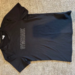Svart t-shirt från Gymshark - Säljer en svart t-shirt från Gymshark med tryckt logga i vitt på bröstet. Klassisk passform med rund hals och korta ärmar. Perfekt för träning eller en avslappnad stil.