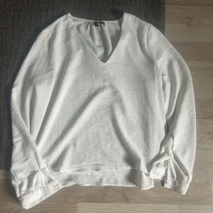 Vit v-ringad blus från Vero Moda - Säljer en stilren vit blus från Vero Moda med v-ringning och långa ärmar. Blusen har knappar vid ärmsluten. Perfekt för en fräsch och enkel look. Säljer för den är liten.