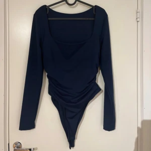 Mörkblå långärmad bodysuit - Säljer en mörkblå långärmad bodysuit med fyrkantig ringning. Bodyn har en åtsittande passform och är tillverkad i ett stretchigt material. Perfekt att styla med jeans eller kjol för en trendig look.