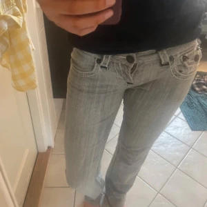 Grå jeans med broderade fickor - Snygga grå lågmidjade jeans med broderade detaljer på bakfickorna. De har en klassisk femficksdesign och en knappgylf. De är köpta från Vinted och vet inte märket de kommer från💕