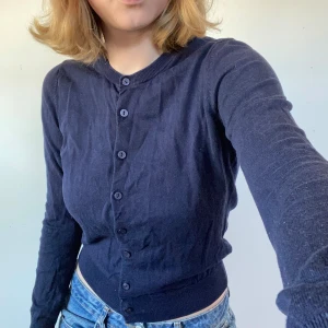 Mörkblå kofta från Uniqlo - Säljer en klassisk mörkblå kofta från Uniqlo i mjukt bomullsmaterial. Koftan har rund halsringning, långa ärmar och knäppning framtill med matchande knappar. Perfekt att styla till jeans eller kjol.