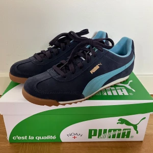 Puma x NOAH Arizona, strl 38,5 - Superfina skor, modell 396056 01. Unisex-storlek 38,5. Navy/blå med gummisula.   Stilren retro-löparstil från Pumas samarbete med NOAH. Skorna har snörning, extra ljusblå skosnören och en cool retrovibe. Den lilla flärpen framtill är avtagbar med kardborre, så du kan själv välja om du vill ha den på eller av.  Helt i nyskick, lite fel storlek för mig. Säljes med originalkartong. Nypris ca 1300–1500 kr. Den här färgkombon är svår att få tag på i butik idag.  Kolla gärna in mina andra annonser! /K