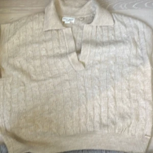 Beige kabelstickad polotröja Holly & Whyte. - Kabelstickad beige polotröja från Holly & Whyte by Lindex. Tröjan har klassisk krage med v-ringning och ribbade muddar. Mjuk och skön, perfekt för lager-på-lager. Passar dig som gillar en clean och tidlös stil.