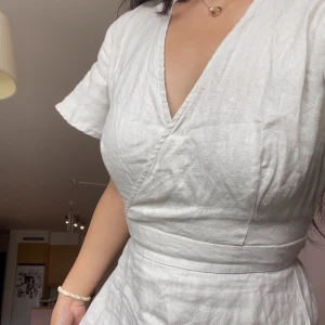 Vit skjorta i 100% linne – NA-KD - Superfin vit kortklänning från NA-KD i linne med omlott och v-ringning. Klänningen har korta ärmar, markerad midja och knytning i ryggen. Perfekt för varma dagar när du vill känna dig både chill och snygg.