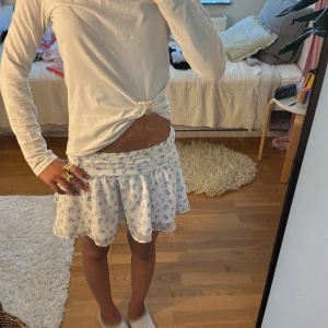 Vit blommig kortkjol med volang - Supersöt vit kortkjol med blått blommönster och bred, rynkad midja. Den har storlek 134-140 men är ganska stretchig och passar mig som är 154cm ifall man gillar korta kjolar. Jag säljer den pga den inte har kommit till användning men kom gärna med prisförslag o frågor! 🫶