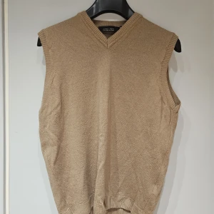 Beige stickad väst från Zara Man - Säljer en stilren beige stickad väst från Zara Man. Västen har v-ringad halsringning och ribbade kanter vid ärmhål och nederkant. Perfekt att bära över en skjorta för en clean look. Enkel och klassisk design utan mönster.