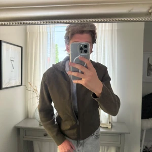 Olivgrön overshirt från Massimo Dutti - Säljer en olivgrön overshirt från Massimo Dutti. Jackan har ribbstickade ärmar och krage, slät framsida med dragkedja och två fickor. Den är i bra skick men den har ett litet hål på ryggen, därav priset. 