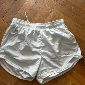 Vita träningsshorts från Nike - Lätta och luftiga ”turkos” träningsshorts från Nike med diskret prickigt mesh-tyg och elastisk midja med snörning. Perfekta för löpning eller gym, med klassisk Nike-logga framtill och snygga detaljer i sidorna för extra ventilation. Använda ca 3 ggr