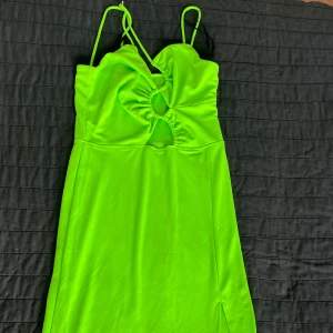 Limegrön långklänning med cut-outs - Snygg limegrön långklänning med smala axelband och unika cut-outs framtill. Klänningen har en slits på sidan och är figurnära med stretchigt material som ger en cool och trendig look. Perfekt för sommarkvällar eller när du vill sticka ut.