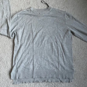 Grå stickad tröja från H&M Basics - En enkel och stilren grå stickad tröja från H&M Basics. Tröjan har rund halsringning med ribbade muddar vid hals, ärmslut och nederkant. Perfekt för lager-på-lager och funkar till alla dina favoritjeans.
