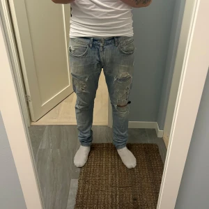 Ljusblå slitna jeans från Dondup - Säljer ett par ljusblå jeans från Dondup med rejält slitna detaljer och hål på både fram- och baksida. Jeansen har klassisk femficksdesign, skinny passform och är tillverkade i jeansmaterial. Perfekta för dig som gillar en edgy och avslappnad stil.