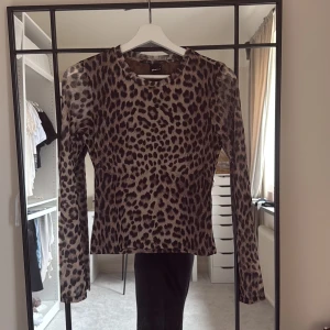 Leopardmönstrad långärmad tröja Glamorous - Säljer en snygg långärmad tröja från Gina tricot med leopardmönster i bruna och svarta toner. Tröjan har en rund halsringning och är figurnära i modellen, perfekt för dig som vill sticka ut lite extra. Materialet är mjukt och stretchigt för en bekväm passform.