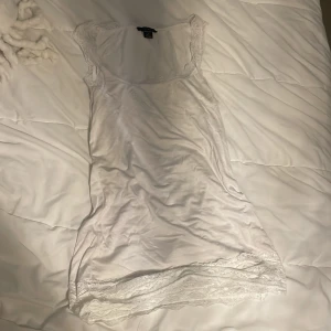 Vit spetskantad linnetopp från MQ - Supersöt vit linnetopp från MQ med breda axelband och fina spetsdetaljer längs både ringning och nederkant. Tunt och mjukt material som känns skönt mot huden. Perfekt att styla lager på lager eller som den är under varma dagar.