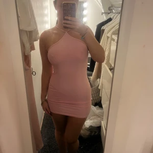 Rosa tight kortklänning  - Säljer en ljusrosa, tight och kort klänning med halterneck och smala axelband som korsas framtill. Klänningen är ärmlös och har en enkel, stilren design som sitter figurnära.🩷🩷