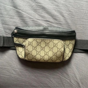 Mönstrad midjeväska - Snygg midjeväska med ett klassiskt mönster och svarta detaljer. Väskan har flera dragkedjeförsedda fack och en justerbar rem för bekväm passform. Perfekt för att hålla dina saker säkra och nära till hands.