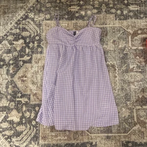 Lila rutig kortklänning H&M Divided - Supersöt lila och vit rutig kortklänning från H&M Divided. Klänningen har smala axelband och en lätt utsvängd passform. Perfekt för varma dagar och ger en fräsch sommarkänsla. Tunt och luftigt material som känns skönt mot huden.