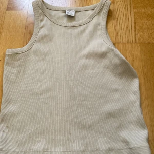 Beige ribbad linnetopp från Lindex - Säljer en stilren beige ribbad linnetopp från Lindex i storlek 146/152. Toppen är ärmlös med klassisk rund halsringning och har en tight passform. Perfekt för varma dagar eller som lager under en skjorta. Enkel och clean look som passar till allt. Dock är det två fläckar nere på tröjan.