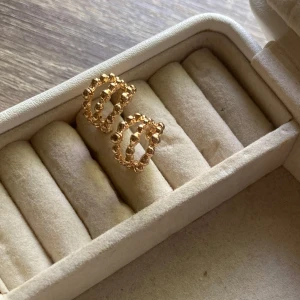 Två par örhängen för 25kr - Priset kan diskuteras !                 Säljer två par örhängen i inte ekta guldton. Ena paret är chunky hoops med slät, blank yta och rund form. Det andra paret har en cool, bubblig design med små kulor som bildar en öppen ring. Perfekta för att mixa och matcha för en trendig look.