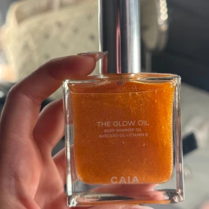 CAIA The Glow Oil Shimmerolja - The Glow Oil från CAIA är en skimrande kroppsolja med avokadoolja och vitamin E. Oljan har en varm, gyllene orange färg med massor av glow och kommer i en snygg fyrkantig glasflaska med silvrig pump. Perfekt för att ge huden en solkysst look. endast testad 