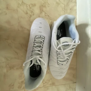 Nike Air Max Plus vita sneakers - Nike Air Max Plus i helvitt med mesh-överdel och klassiska vågiga detaljer. Snygg Tn-logga bak och synlig Air Max-dämpning i sulan. Skorna har snörning och en sportig vibe, perfekt för dig som gillar streetstyle och vill sticka ut.