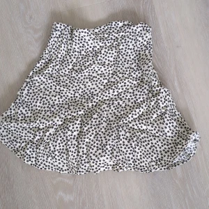 Vit blommig kortkjol från Zara - Supersöt kortkjol/shorts från Zara i vit med små svarta blommor. Kjolen har shorts under, volangkant och smock i midjan för en bekväm passform. Perfekt för dig som gillar en lekfull och trendig stil.